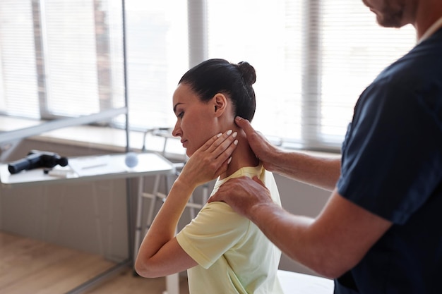 Young woman complaining of neck pain while doctor examining her in hospital