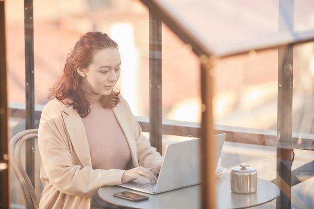 Giovane donna concentrandosi sul suo lavoro in linea digitando sul computer portatile mentre era seduto in un caffè