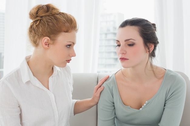 young woman consoling female friend sitting on sofa