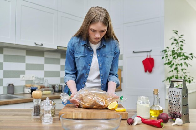 Молодая женщина готовит запеченную курицу в рукаве для выпечки со специями