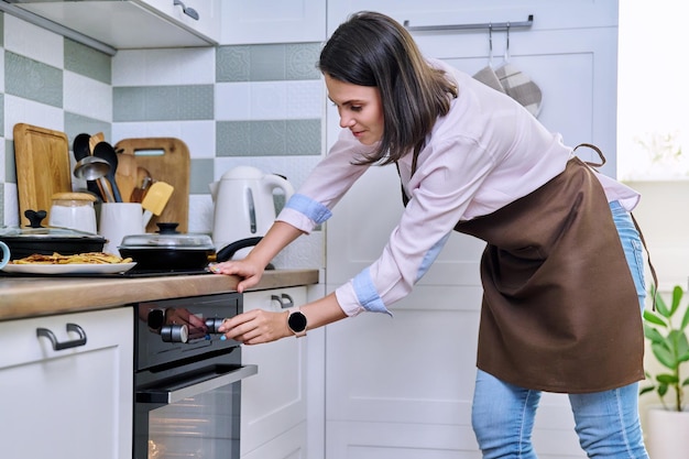 Young woman cooking food in the oven at home in the kitchen Female in an apron using the oven to cook food