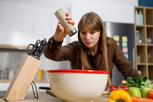 Photo young woman cooking in the kitchen adding pepper into the bowl