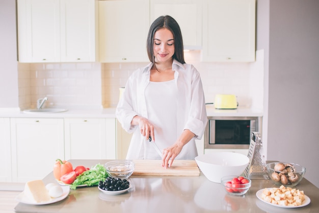 若い女性が台所で料理。彼女は立って野菜を切ります。