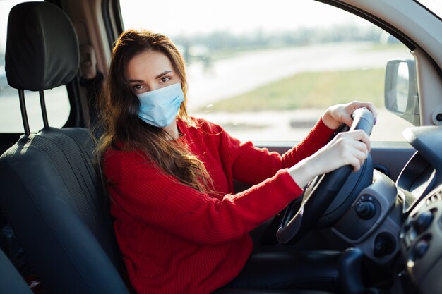 車に座っているコロナウイルスマスクの若い女性