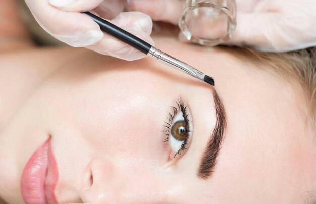 Young woman correcting eyebrow shape with brush, closeup