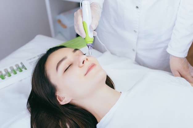 A young woman in the cosmetologists office receives fractional mesotherapy for her face