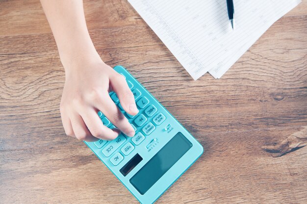 Photo young woman counts on calculator and makes notes on papers