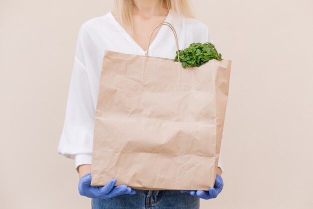 Young woman courier volunteer wearing a protective mask holds a paper bag with products