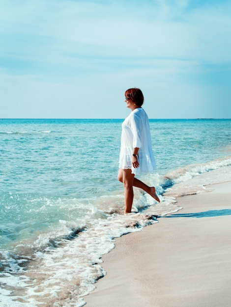 Молодая женщина в прикрытии играет с морскими волнами на пляже. Концепция путешествий и каникул.