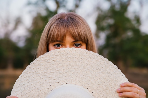 The young woman covered her face with her hat The beautiful eyes of the girl are visible from behind the hat Straw summer hat fashion accessory The concept of summer holidays