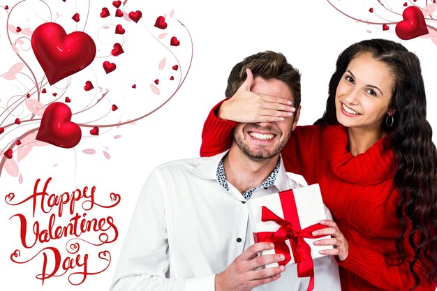 Photo young woman covering eyes of partner holding gift against happy valentines day