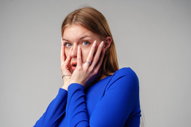 Young woman covering face with hands against gray background