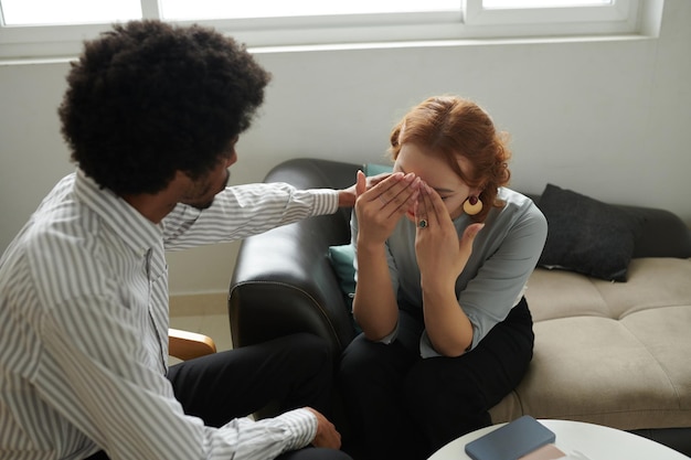 Young woman covering her face with hands when crying talking to her therapist