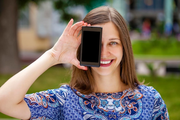 Photo young woman covers her face screen smartphone on a background of the city