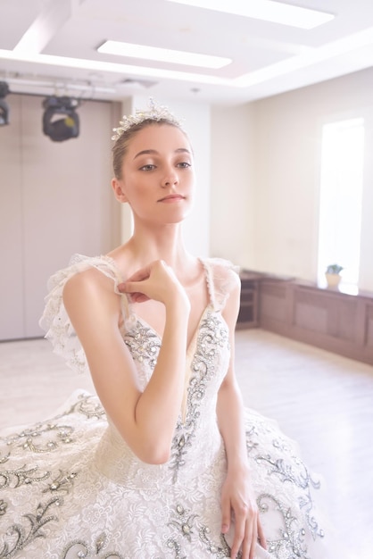 A young woman in a creamcolored dress wearing a crown is putting on her makeup in front of the mirror The concept of beauty