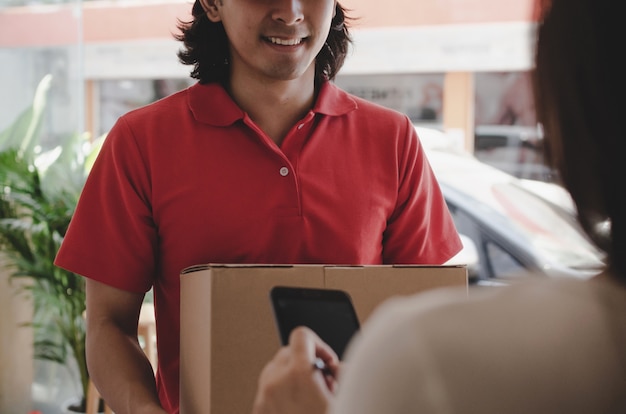 Young woman customer appending signature in digital mobile phone receiving parcel post box from courier