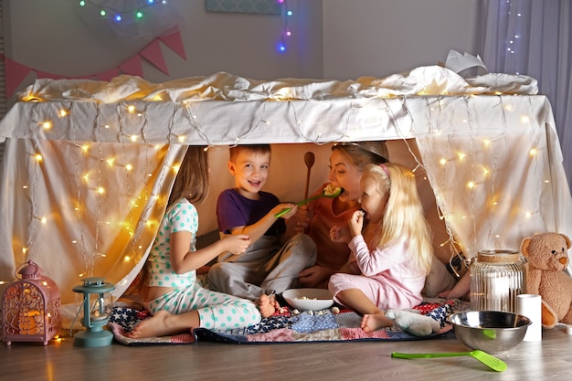 Young woman and cute children playing in hovel at home