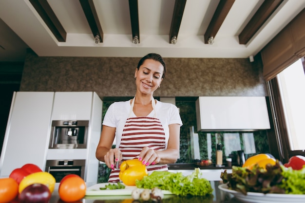 The young woman cuts vegetables in the kitchen with a knife