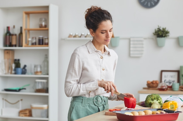 Young woman cutting red pepper on cutting board she preparing dinner in the domestic kitchen