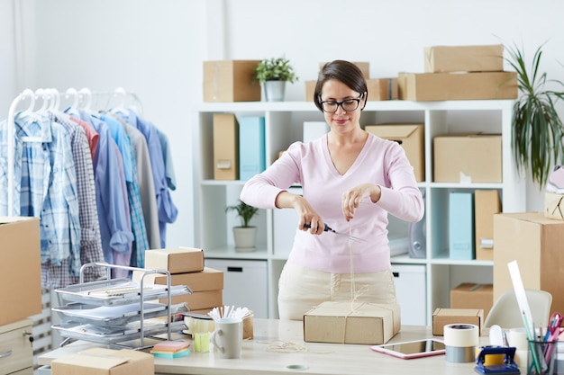 Young woman cutting thread on top of bound parcel