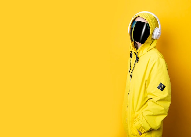 Young woman in cyberpunk glasses mask with headphones in a yellow jacket on a yellow background