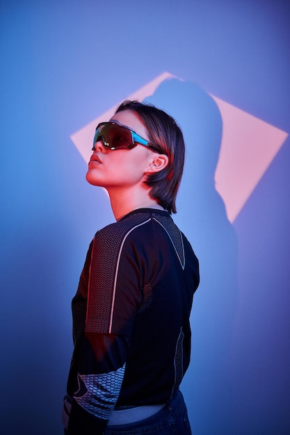 Young woman in cyberpunk role is posing for photographer in blue and red lights.