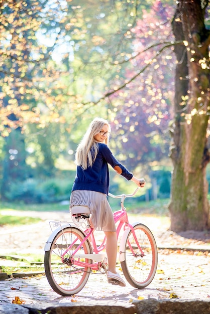 Молодая женщина, езда на велосипеде розовый леди вдоль солнечной мощеной аллее парка
