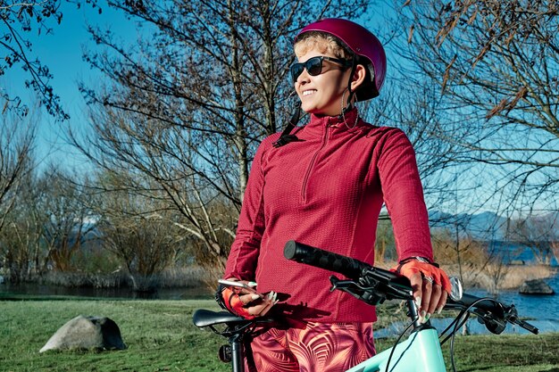 Young woman cyclist with her bike using her mobile phone in a nature park