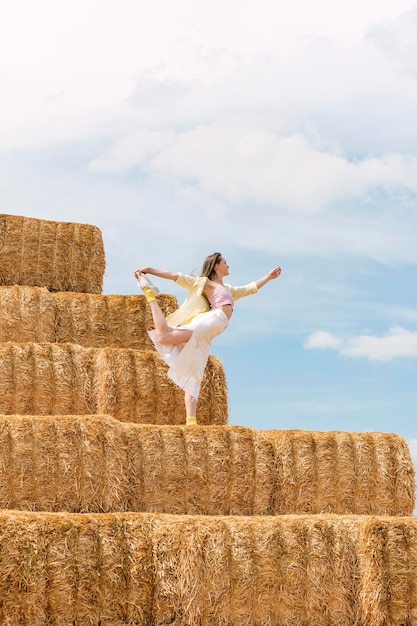 Young woman dances on huge block of hay Hay harvesting for autumn Girl practicing yoga on haystack