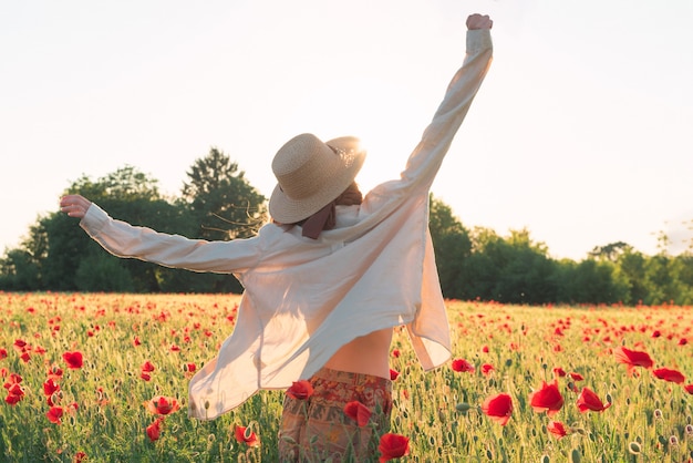 Young woman dancing on poppy field from back in sunset