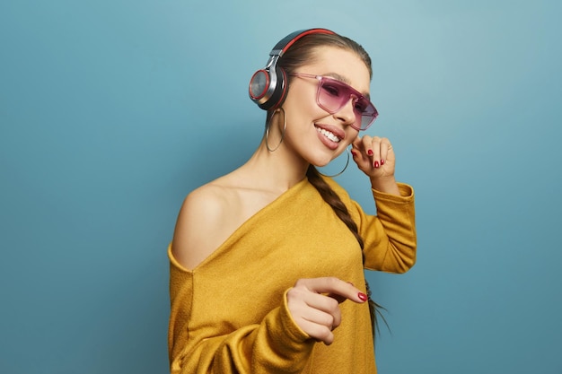 Young woman dancing while listening music with headphones isolated over blue background