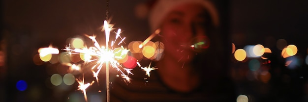 Young woman in dark holds lit sparklers in her hands