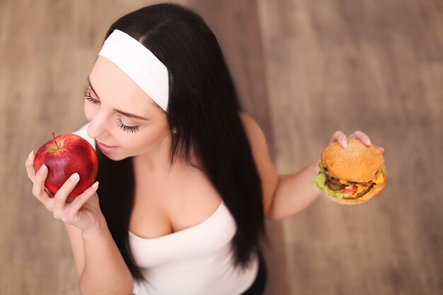 Photo a young woman decides between hamburger and apple