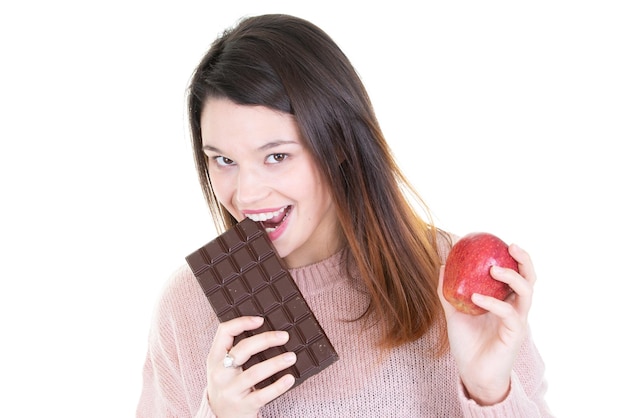 Young woman deciding between chocolate bar eating apple