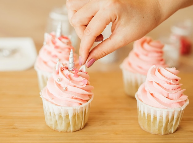 写真 若い女性はカップケーキを飾ります ユニコーン スタイル ピンク色 子供のパーティーのための美しい御馳走