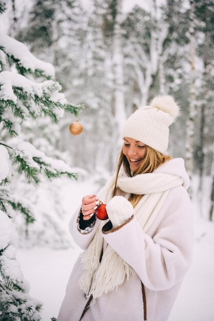 雪の冬の森で赤い宝石で杉の木を飾る若い女性