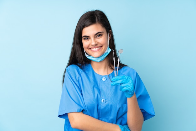 Young woman dentist holding tools over blue wall laughing