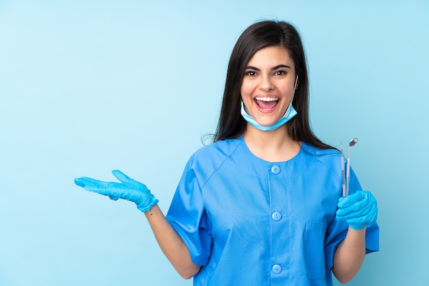 Dentista della giovane donna che tiene gli strumenti sopra la parete blu isolata che tiene il copyspace immaginario sul palmo