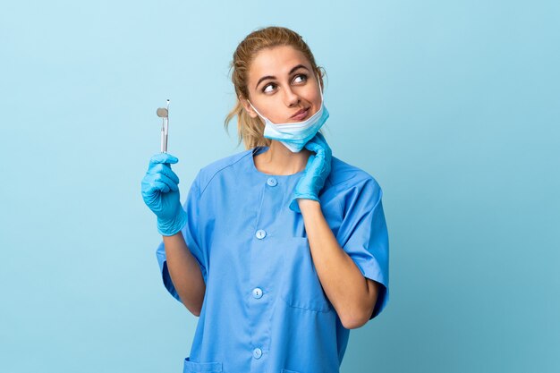 Strumenti di tenuta del dentista della giovane donna sopra la parete blu isolata che pensa un'idea