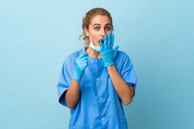 Young woman dentist holding tools over isolated blue with surprise facial expression