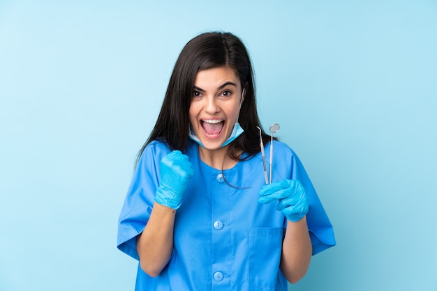 Young woman dentist holding tools over isolated blue