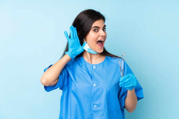 Young woman dentist holding tools over isolated blue