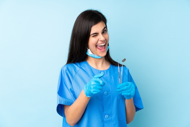 Young woman dentist holding tools over isolated blue