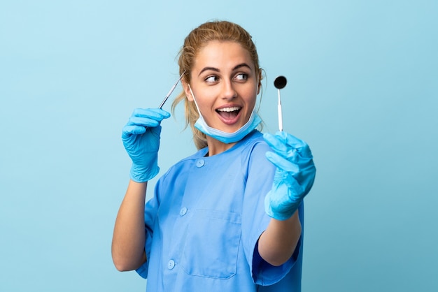 Young woman dentist holding tools over isolated blue