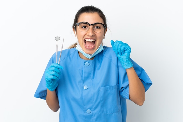 Dentista della giovane donna che tiene gli strumenti isolati su priorità bassa bianca che celebra una vittoria nella posizione del vincitore