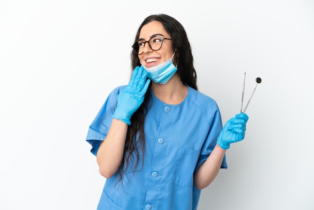 Young woman dentist holding tools isolated on white background looking up while smiling