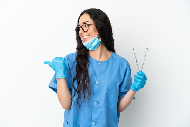 Dentista della giovane donna che tiene gli strumenti isolati su priorità bassa bianca che indica al lato per presentare un prodotto