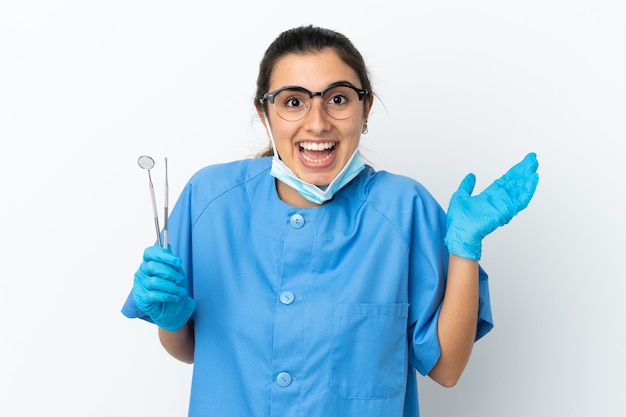 Strumenti della tenuta del dentista della giovane donna isolati su fondo bianco con l'espressione facciale colpita