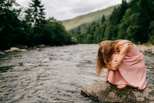 Young woman in depression sitting at stone in the river