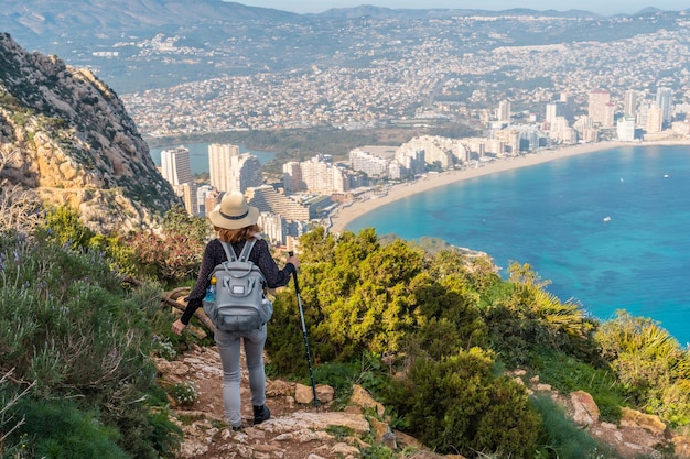 A young woman descending from the top of the Penon de Ifach Natural Park with the city of Calpe in the background Valencia Spain Mediterranean sea View of La Fossa beach